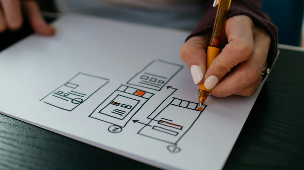 Hand sketching a user interface layout with a pen, testing how sections fit together