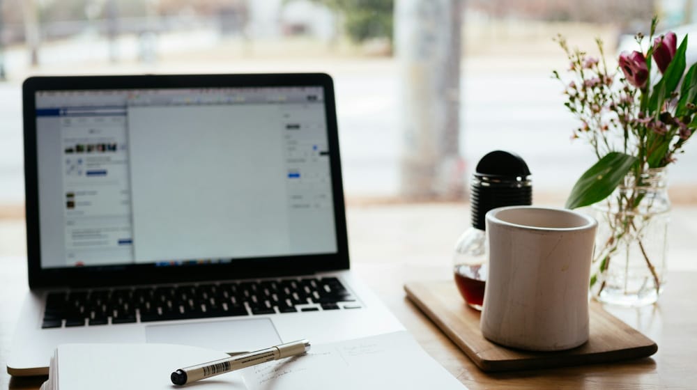 Laptop and coffee mug on a table beside flowers, a calm setup for editing WordPress content