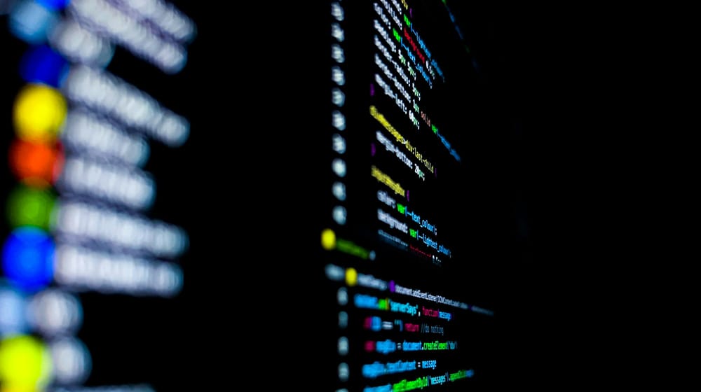 Close-up of screens of code lit by coloured lights, showing React component source files