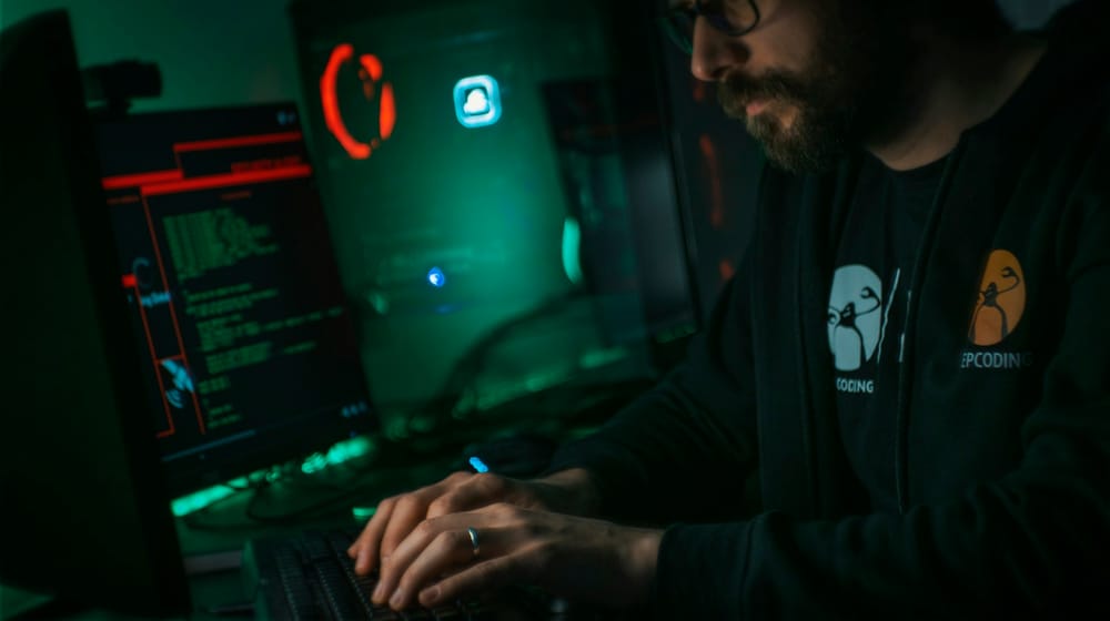 Person working at a computer in a dark room, monitoring a website for security issues