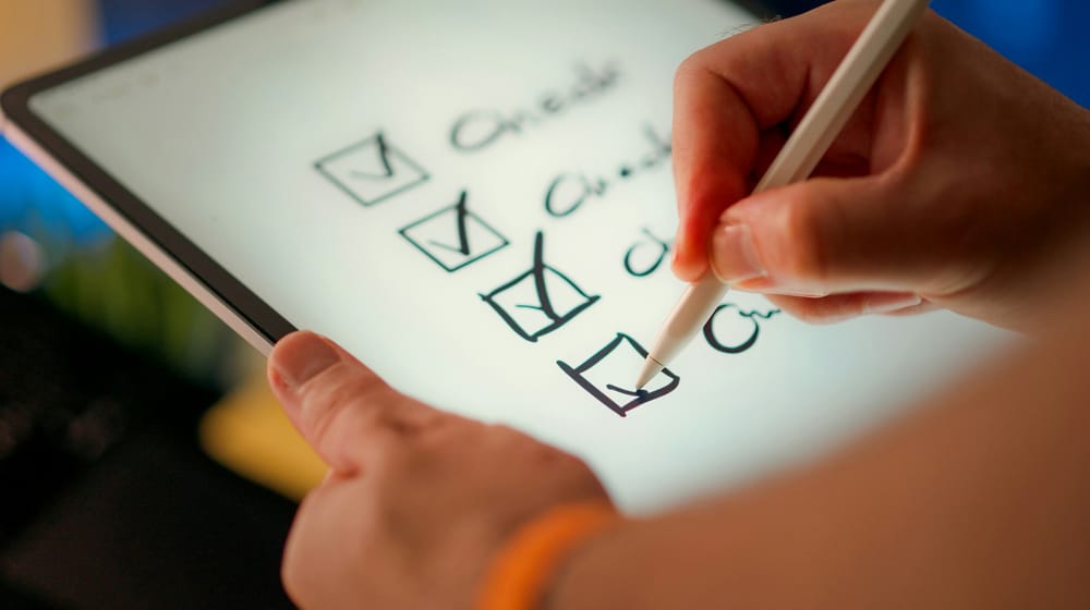 Hand ticking off a checklist on a tablet with a stylus during a plugin audit